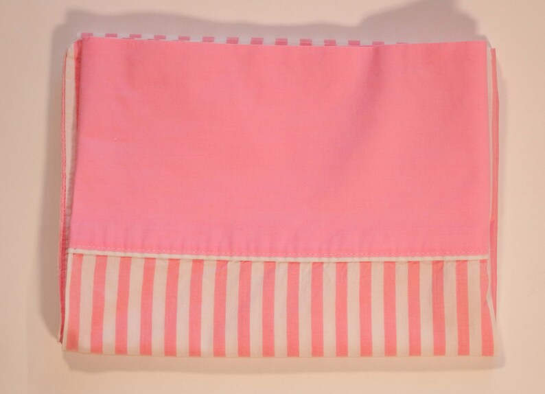 May include: Pink and white striped fabric with a solid pink panel. The fabric is folded in half.
