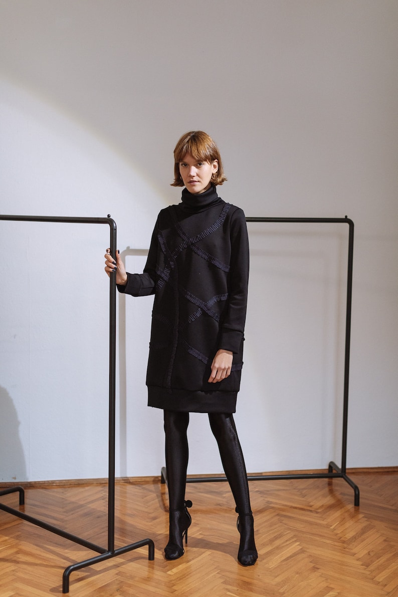 May include: A black turtleneck dress with a long sleeve and a geometric design. The dress is made of a soft, comfortable fabric and has a relaxed fit.