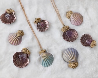 May include: A set of nine gold and iridescent seashell necklaces. The shells are in various shades of pink, purple, blue, and gold. Each shell has a gold accent at the top.