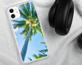 May include: A clear phone case with a tropical palm tree design. The case is on a white fuzzy surface with black headphones.