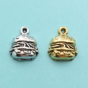 May include: Two silver and gold charm pendants shaped like hamburgers. The charms are detailed with sesame seeds on the bun and lettuce and tomato inside.
