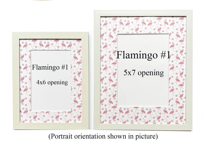 May include: Two white picture frames with flamingo-patterned borders. The frames have openings for 10x15 cm and 13x18 cm photos, with the text "Flamingo #1" on each. The image is in portrait orientation.