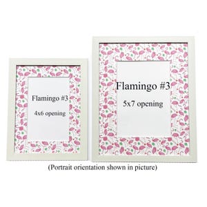 May include: Two white picture frames with a flamingo pattern border and white openings. The frames are labelled "Flamingo #3" with 10x15 cm and 13x18 cm openings. The text "(Portrait orientation shown in picture)" is below the frames.