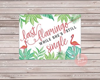 May include: A white sign with green tropical leaves and pink flamingos. The sign says "last flamingo while she's still single".