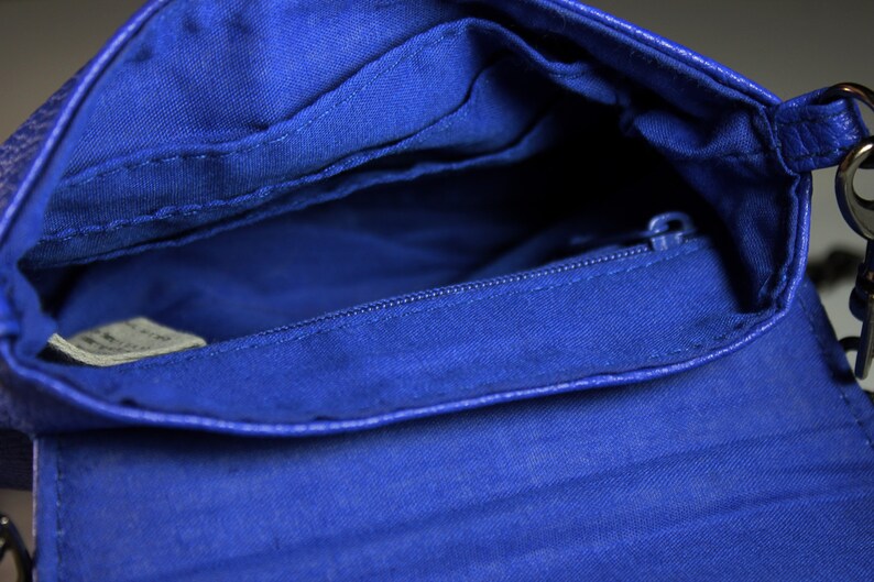 Pode incluir: Vista aberta de uma bolsa transversal azul cobalto. O interior apresenta um bolso com z&iacute;per e forro de tecido. O exterior da bolsa tem uma apar&ecirc;ncia texturizada. A al&ccedil;a de corrente &eacute; vis&iacute;vel no lado direito.