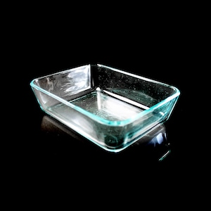 May include: A clear glass baking dish with a light blue rim. The dish is empty and sitting on a black surface.