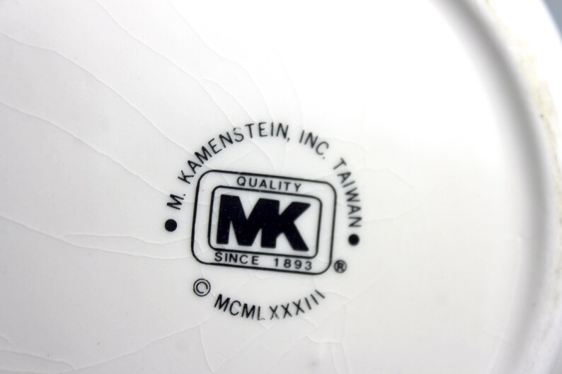 May include: A white ceramic plate with a black and white logo that reads "M. Kamenstein, Inc. Taiwan Quality MK Since 1893 &copy; MCM LXXXXIII"