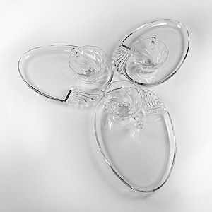 Puede incluir: Juego de tazas de té y platillos de vidrio transparente. Cada platillo ovalado tiene un diseño decorativo. Las tazas de té tienen un diseño en espiral y un asa. El juego está dispuesto en un patrón circular sobre una superficie blanca.