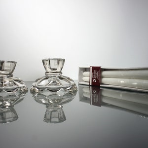 Puede incluir: Dos candelabros de cristal transparente con base festoneada y una caja de dos velas de t&eacute; blancas. La caja tiene una etiqueta roja y blanca que dice "Velas de t&eacute; 2 unidades".