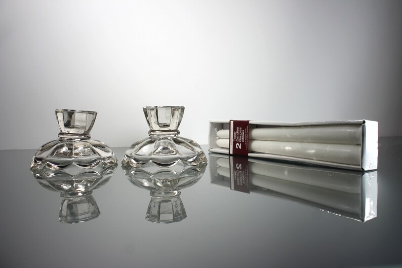 Puede incluir: Dos candelabros de cristal transparente con base festoneada y una caja de dos velas de t&eacute; blancas. La caja tiene una etiqueta roja y blanca que dice "Velas de t&eacute; 2 unidades".
