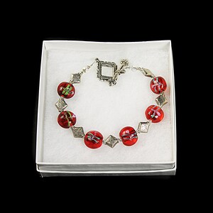 May include: A red glass bead bracelet with silver accents and a silver clasp. The beads are round and have a swirl design.