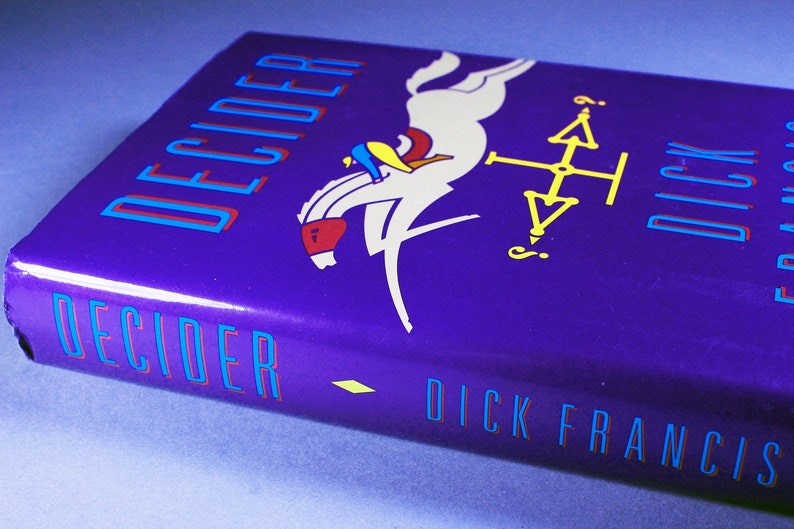 May include: A purple hardcover book with the title "DECIDER" in blue and red lettering. The book cover features a white horse jumping over a yellow compass with a question mark. The author's name, "DICK FRANCIS", is printed in blue and red lettering at the bottom of the cover.