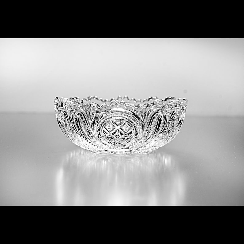 Pu&ograve; includere: Una ciotola di vetro trasparente con intricati motivi incisi. La ciotola ha un bordo smerlato e un disegno a forma di diamante al centro. Probabilmente &egrave; destinata a servire o esporre.