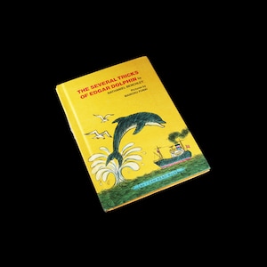 May include: A yellow book cover with a cartoon illustration of a dolphin jumping out of the water. The book title is "The Several Tricks of Edgar Dolphin" by Nathaniel Benchley. The book is an "I Can Read Book" and illustrated by Mamoru Funai.