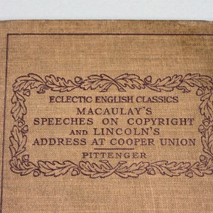 Op de afbeelding: Een bruin boek met een decoratieve rand van eikenbladeren en eikels. De titel luidt "Eclectic English Classics Macaulay's Speeches on Copyright and Lincoln's Address at Cooper Union Pittenger".