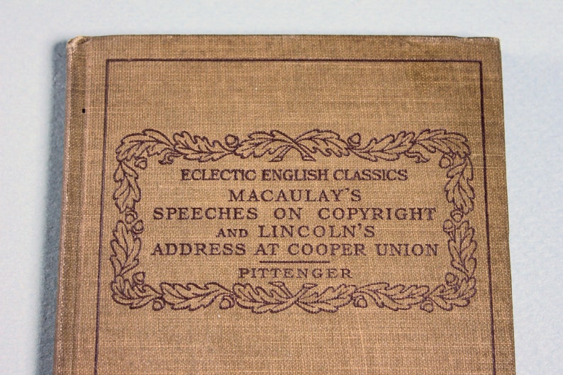 Op de afbeelding: Een bruin boek met een decoratieve rand van eikenbladeren en eikels. De titel luidt "Eclectic English Classics Macaulay's Speeches on Copyright and Lincoln's Address at Cooper Union Pittenger".