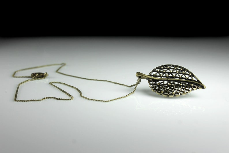 May include: A gold chain necklace with a delicate, intricate leaf pendant. The leaf is made of metal and has a detailed, openwork design.