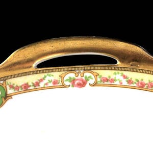 May include: A white porcelain serving dish with a gold rim and a floral design. The dish has a handle on the top.