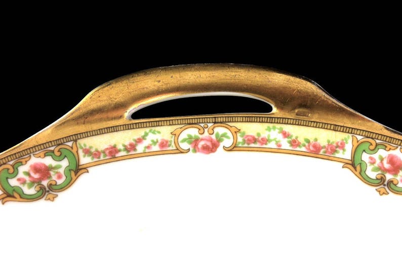 May include: A white porcelain serving dish with a gold rim and a floral design. The dish has a handle on the top.