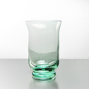 May include: A clear, green-tinted glass with a flared top and a rounded base. The glass has a slightly textured surface and a decorative, circular base. The glass is designed to hold liquids and is suitable for various beverages.