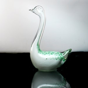 May include: A white glass swan figurine with green flecks throughout. The swan has a long neck and a curved body.