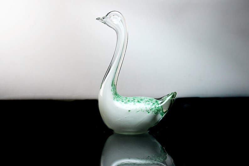 May include: A white glass swan figurine with green flecks throughout. The swan has a long neck and a curved body.