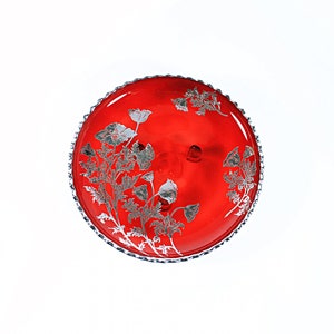 Puede incluir: Un soporte para tartas de vidrio rojo con un diseño floral plateado. El soporte tiene un borde festoneado y es perfecto para exhibir postres.
