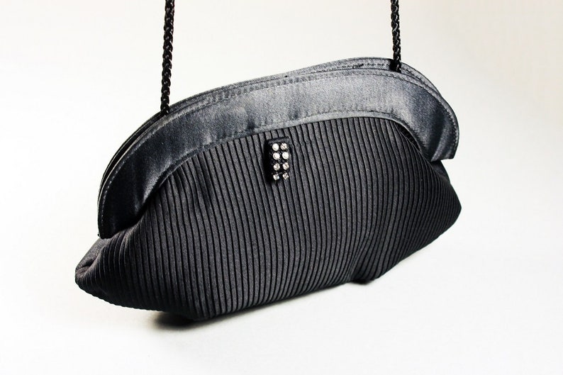 May include: A black satin evening bag with a pleated design and a rhinestone clasp.