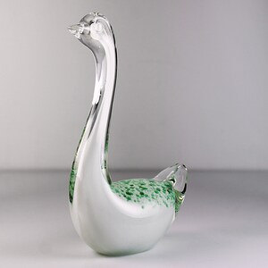 May include: A white glass swan figurine with green speckled accents. The swan has a long neck and a curved body.