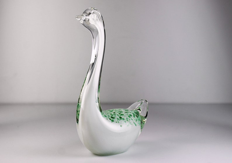 May include: A white glass swan figurine with green speckled accents. The swan has a long neck and a curved body.