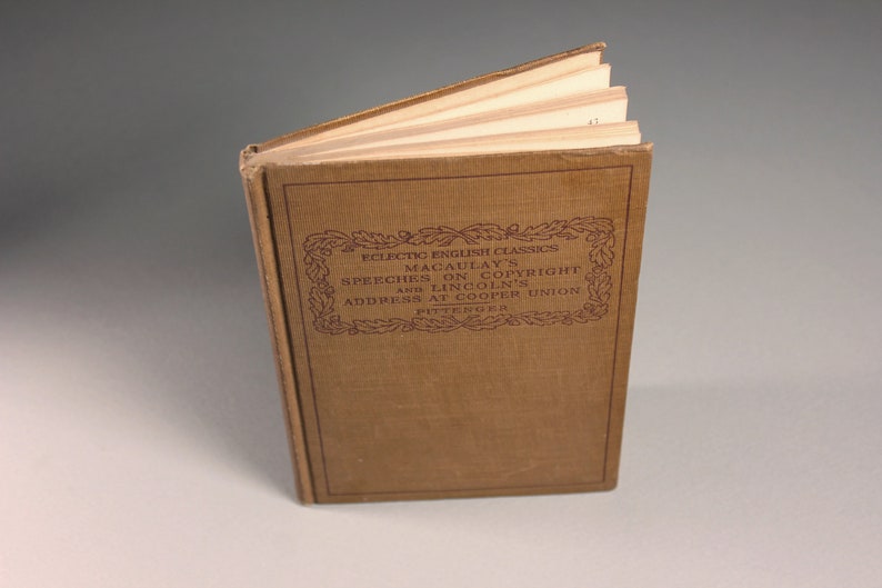 Op de afbeelding: Een bruin boek met de titel "Eclectic English Classics Macaulay's Speeches on Copyright and Lincoln's Address at Cooper Union Pittenger" gedrukt op de omslag.