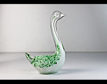 May include: A white glass swan figurine with green speckled accents. The swan has a long neck and a curved body.