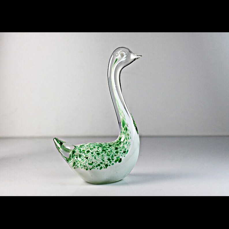 May include: A white glass swan figurine with green speckled accents. The swan has a long neck and a curved body.
