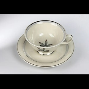 May include: A white teacup and saucer with a silver rim and a green leaf design.