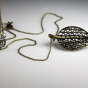 May include: A delicate gold-toned necklace with a leaf pendant. The pendant is made of intricate metalwork and has a delicate, openwork design.