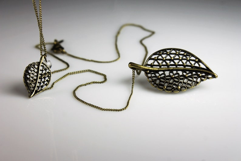 May include: A delicate gold-toned necklace with a leaf pendant. The pendant is made of intricate metalwork and has a delicate, openwork design.