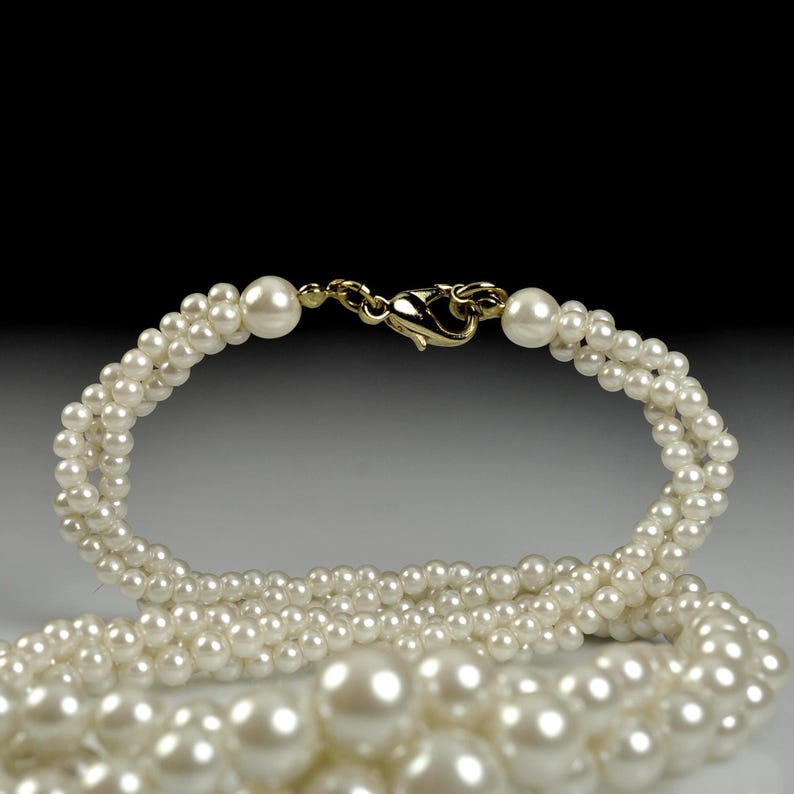 May include: A three-strand pearl necklace with a gold-coloured clasp. The necklace is made up of many small, round, white pearls. The clasp is a simple hook and eye design. The pearls have a lustrous sheen.