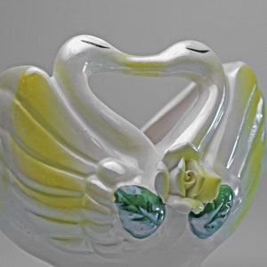 May include: White ceramic swan planter with yellow and green accents. The swans are kissing and have a rose in the center.