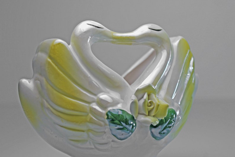 May include: White ceramic swan planter with yellow and green accents. The swans are kissing and have a rose in the center.