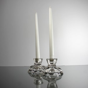 Puede incluir: Dos candelabros de cristal transparente con velas blancas. Los candelabros tienen un dise&ntilde;o decorativo festoneado.