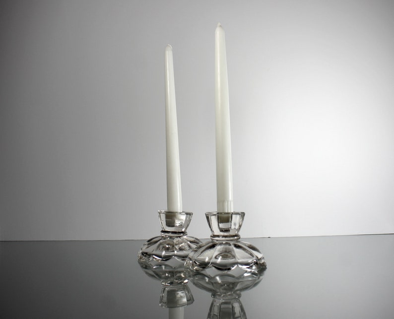 Puede incluir: Dos candelabros de cristal transparente con velas blancas. Los candelabros tienen un dise&ntilde;o decorativo festoneado.