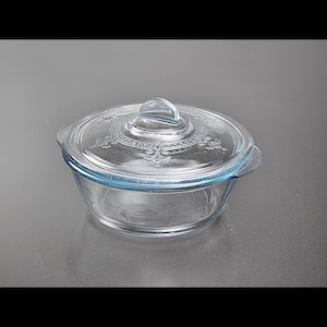 Puede incluir: Un plato para hornear de vidrio transparente con tapa. El plato tiene un borde azul claro y la tapa tiene un patrón decorativo.