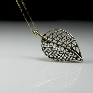 May include: A gold leaf pendant necklace with a delicate, intricate design. The pendant is made of metal and has a chain attached to it.