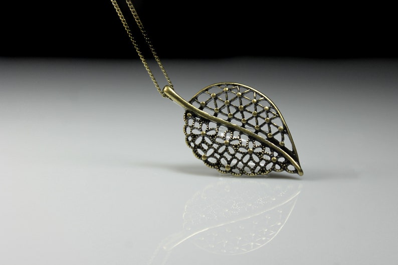 May include: A gold leaf pendant necklace with a delicate, intricate design. The pendant is made of metal and has a chain attached to it.