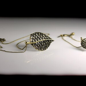 May include: A gold necklace and earrings set featuring a delicate leaf design. The leaves are made of a fine, intricate metalwork and have a slightly oxidized finish.