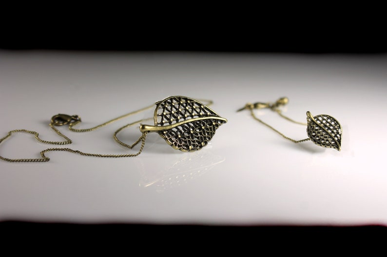 May include: A gold necklace and earrings set featuring a delicate leaf design. The leaves are made of a fine, intricate metalwork and have a slightly oxidized finish.