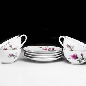 Peut inclure: Un ensemble de quatre tasses &agrave; th&eacute; et soucoupes blanches avec un motif floral repr&eacute;sentant des roses roses et des feuilles vertes.