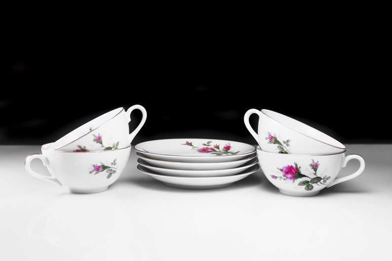 Peut inclure: Un ensemble de quatre tasses &agrave; th&eacute; et soucoupes blanches avec un motif floral repr&eacute;sentant des roses roses et des feuilles vertes.