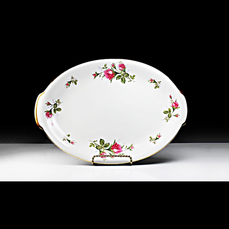 Puede incluir: Plato de servir ovalado blanco con borde dorado y un delicado patr&oacute;n floral de rosas rosas y hojas verdes.