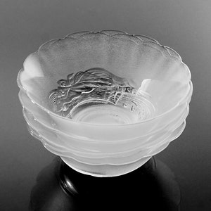 May include: A stack of frosted glass bowls with a scalloped rim. The bowls have a detailed, raised design in the center. The bowls are stacked on top of each other, creating a layered effect. The bowls are likely for serving.